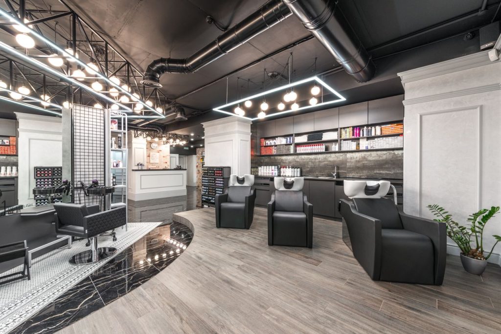 Comfortable backwash chairs with sinks near potted plant placed in contemporary beauty salon with bright illumination and abundance of cosmetology products